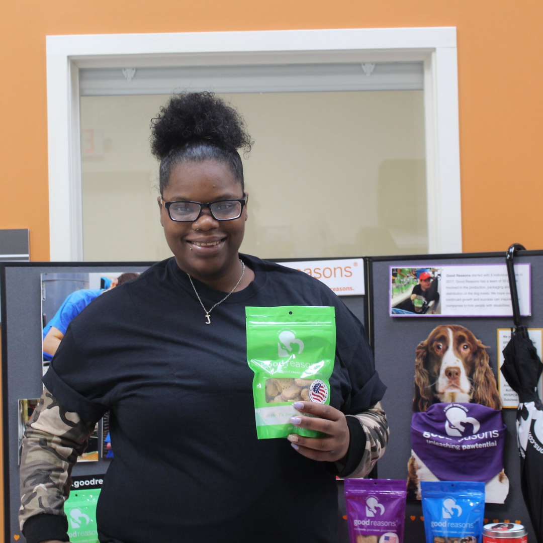 Woman holding green bag of Good Reasons Dog Treats in front of a display