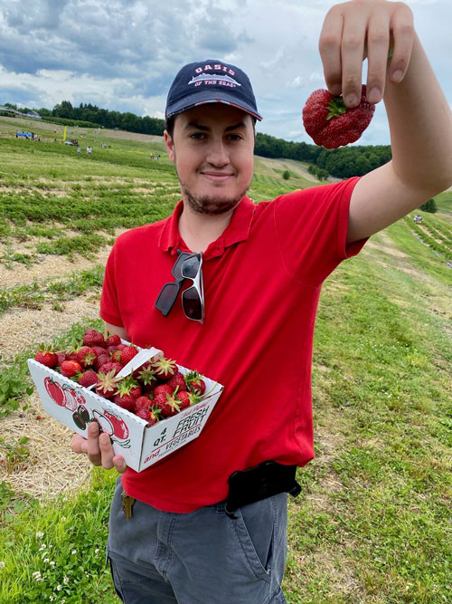 Young man standing in a field and holding strawberries