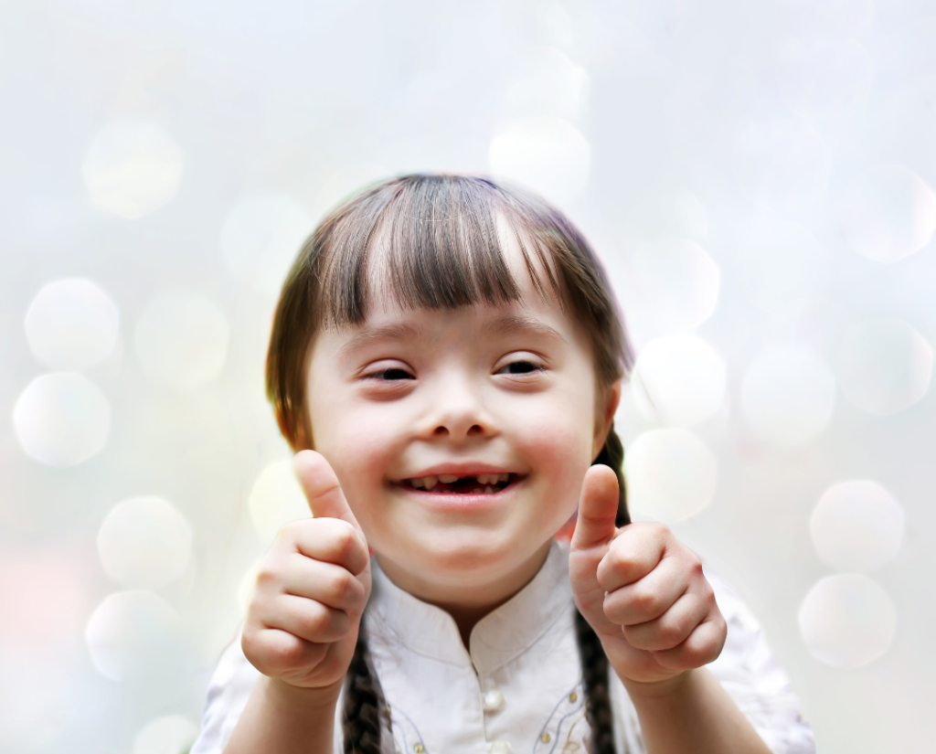 child with down syndrome smiling and holding two thumbs up
