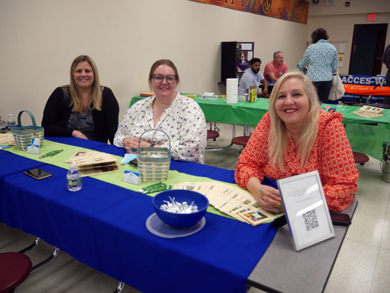 Three Community Based Services staff sit at a table with promotional material in a high school building during a Transition Planning services fair.