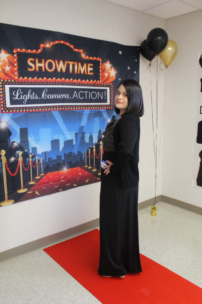 A woman stands in a black dress in front of a movie premiere backdrop