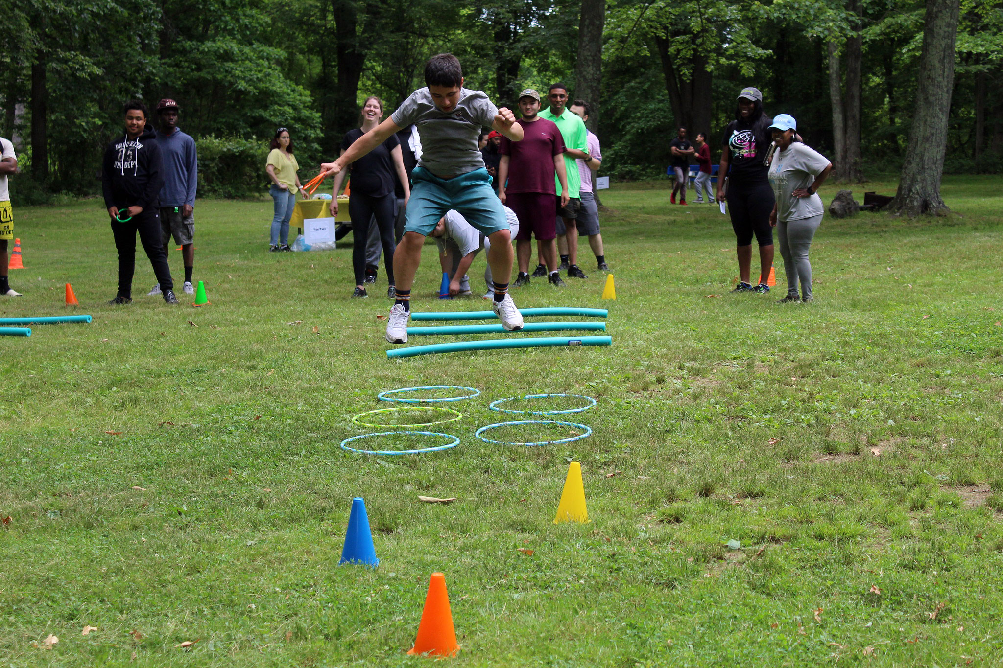 A young man jumps high in the air as he navigates an obstacle course while his friends look on.