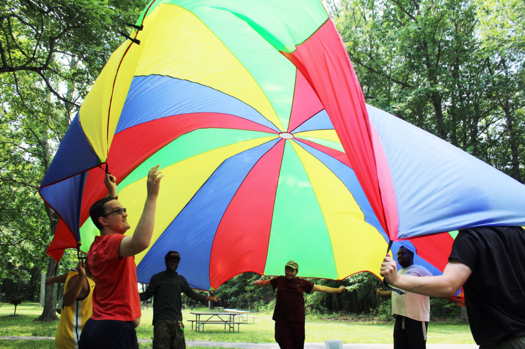a group of young men raise a colorful parachute over their heads at a park