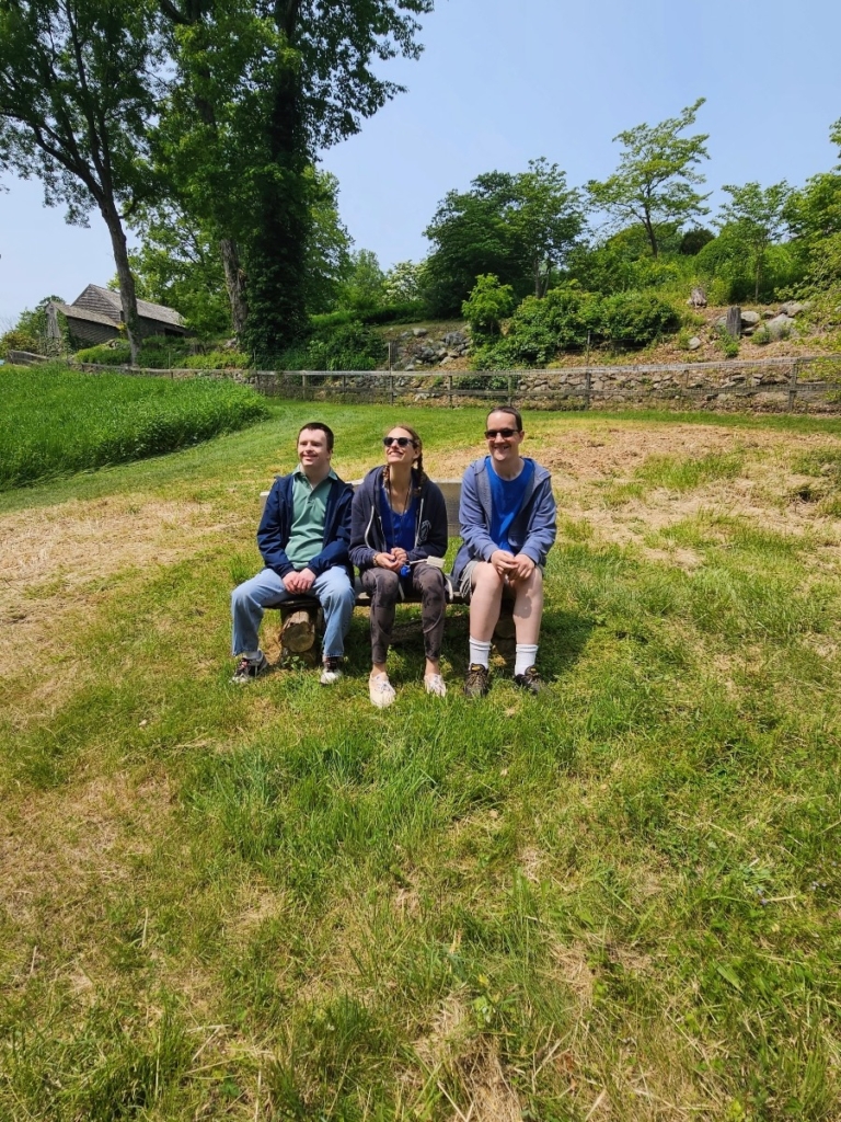 Three people sit on a bench at DIG Farm