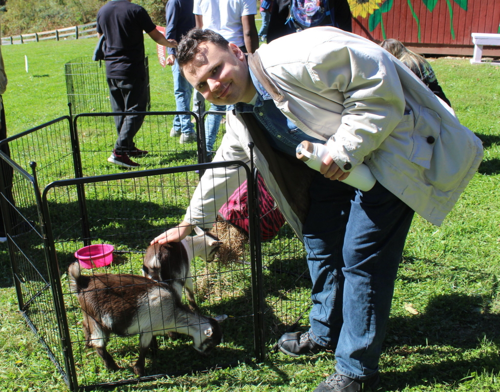 A young man leans over an enclosure to pet two small goats at Cultivating Dreams Farm