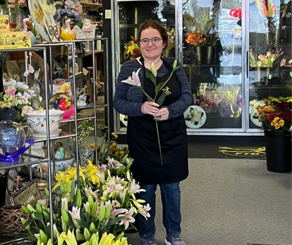 A woman stands in a florist and gift shop holding a lily
