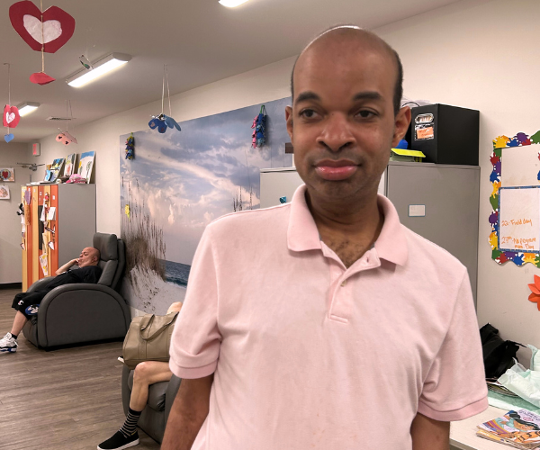 A man stands in the Site Based day hab room in front of a mural of a beach and two massage chairs. Heart mobiles hang from the ceiling.