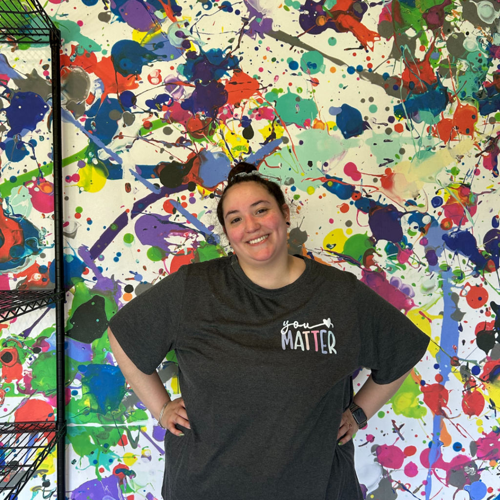 Annie Ayala, a dance and movement teacher, poses in front of an art wall.