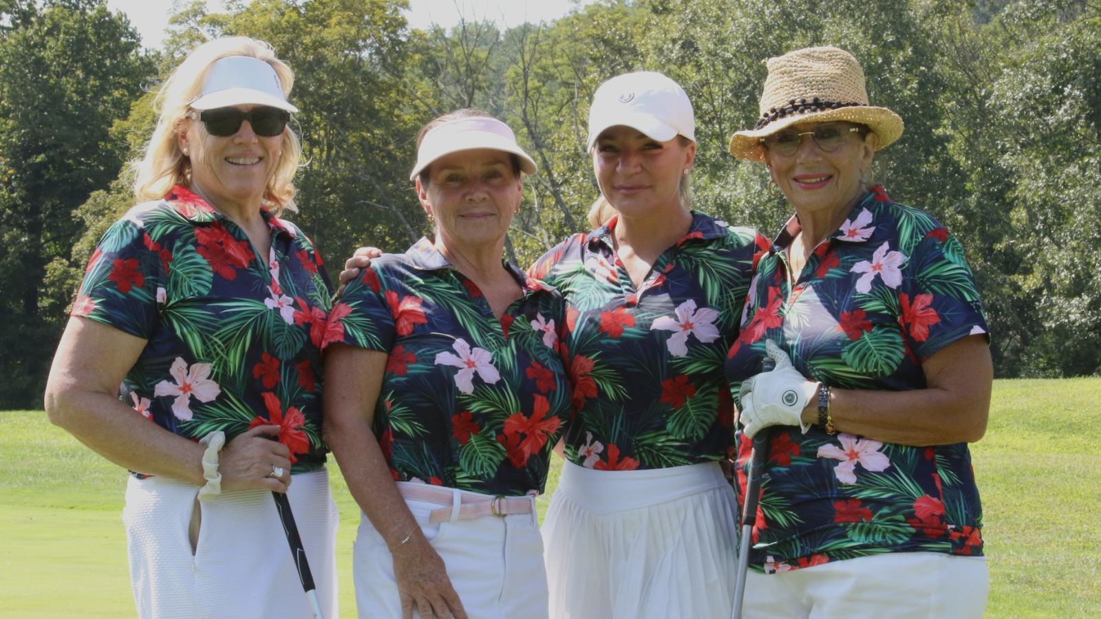 Four ladies, wearing matching floral golf shirts and white golf shorts, hats and visors, pose on the greens of Hollow Brook Golf Club.