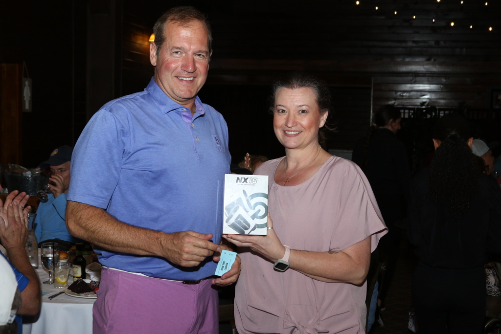 A tall man in a blue golf shirt accepts his raffle prize of a range scope finder