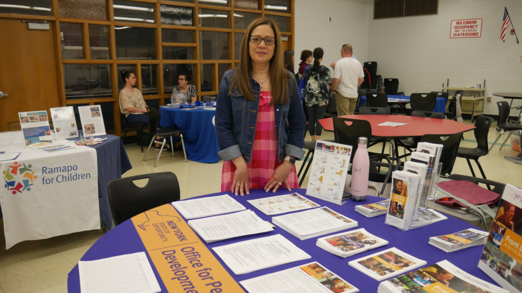 A woman from OPWDD stands by her table laden with information at the CBS Transition Fair