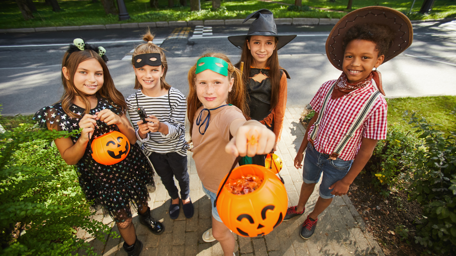 A group of five children dressed in costumes arrive at the entrance of a house and hold out their pumpkin shaped buckets as they trick or treat on Halloween.