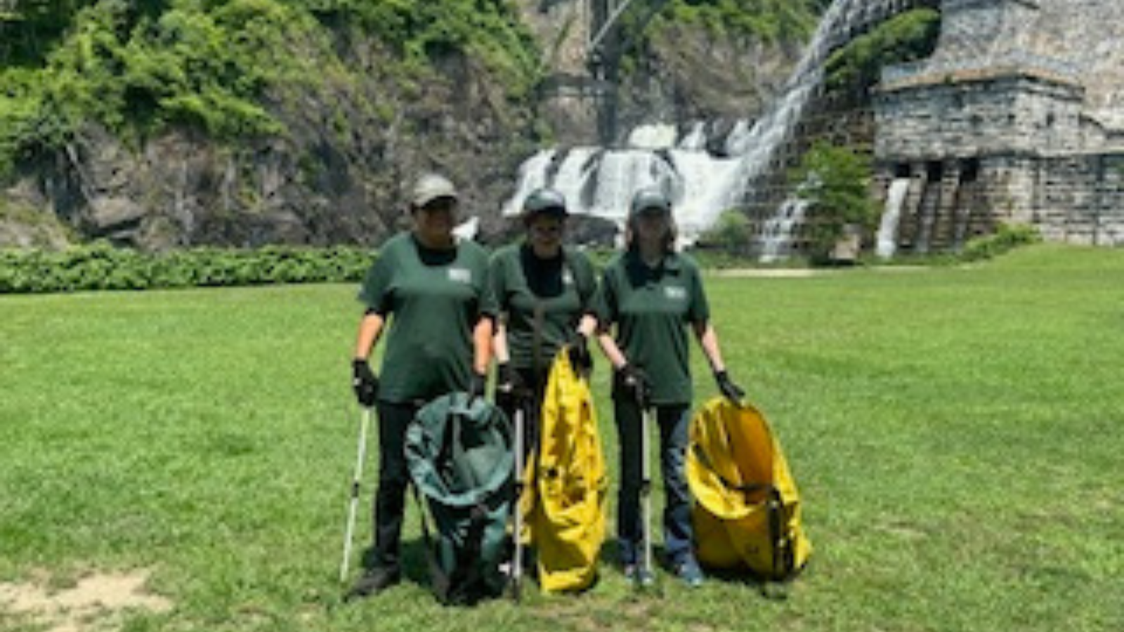 Three workers with Park uniforms work at Croton Point Park NY with garbage picking tools and large sacks.