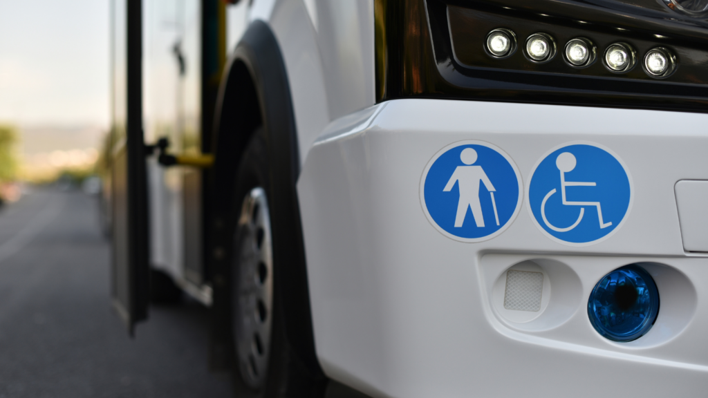 The front bumper of a paratransit bus showing the blue circle stickers with an icon for a person with a cane and an icon of a person in a wheelchair in white.