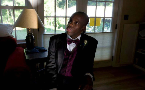 Portrait of Leroy F. Moore, Jr. in a tuxedo with maroon bow tie and vest. He is seated indoors by a lamp and table.