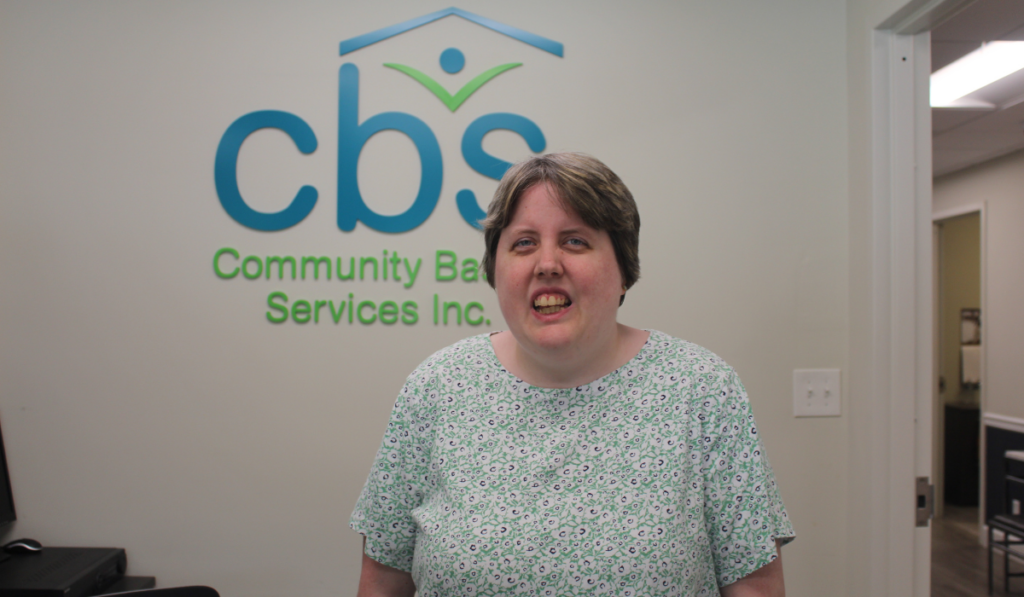 Erin H. Stands in front of the CBS interior sign at her receptionist station.