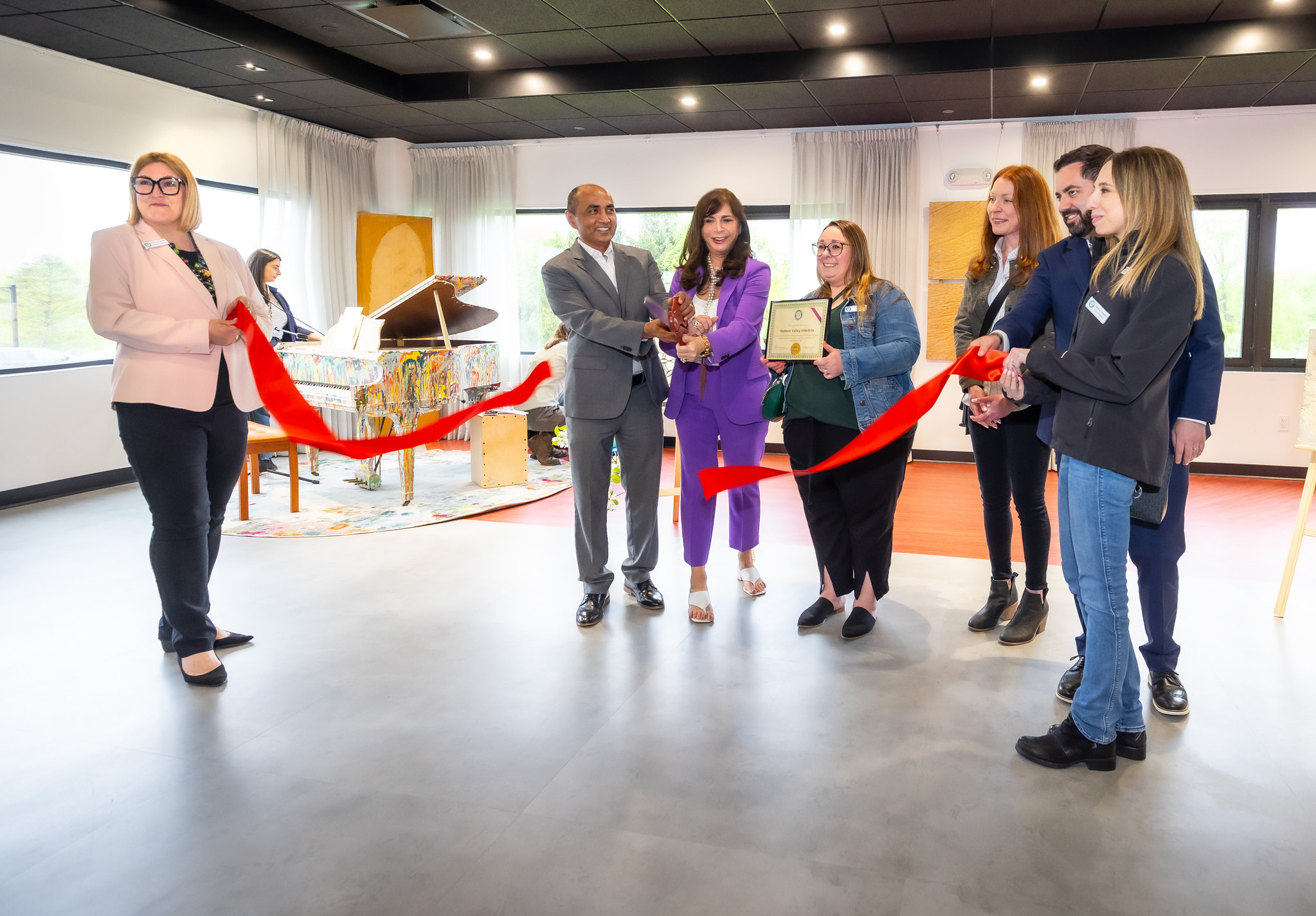 Members of the Brewster Chamber of Commerce stand with CSO Bhakar Singh and CEO Vicki Sylvester, Ph.D. as they cut a large red ribbon in the community room of the InterArts building.