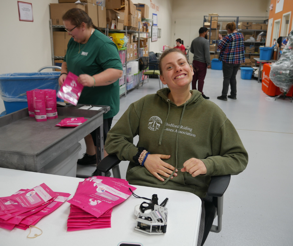 A young woman smiles with pride as she develops work skills while packing dog biscuits into pink Good Reasons bags.