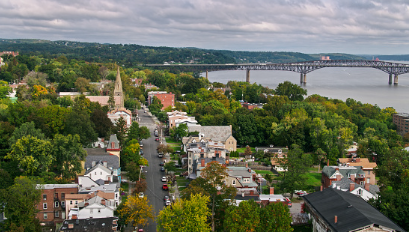 An aerial view of Orange County, tree lined streets by the river with the Newburgh Bridge in the distance.