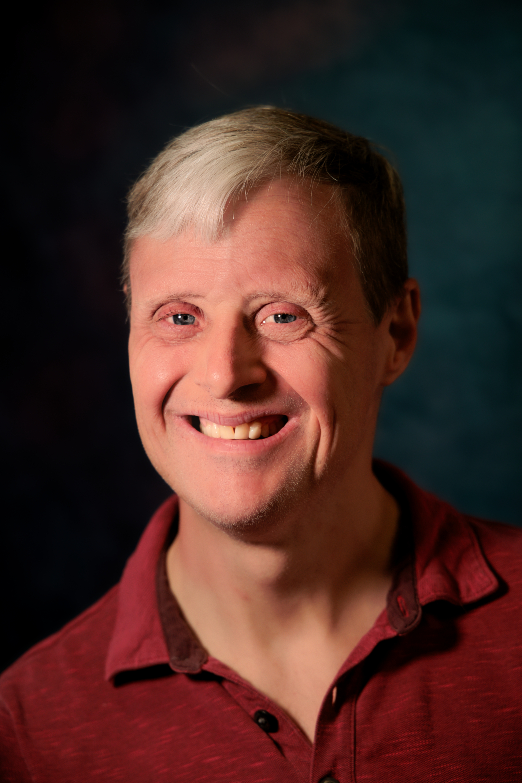 Portrait of Anthony Canale in a maroon polo style shirt on a blue background.