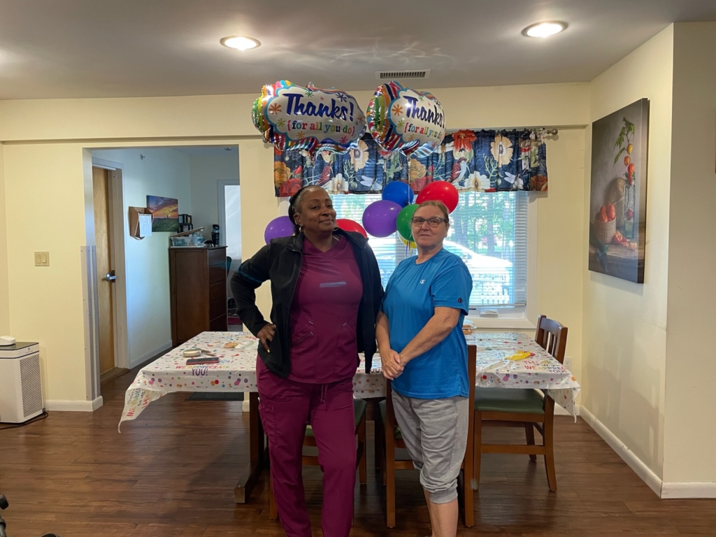 Itasha Ross and Bonnie Peterson, DSPs at CBS stand in front of celebratory balloons in the dining area of the group home where they take card of people with disabilities.