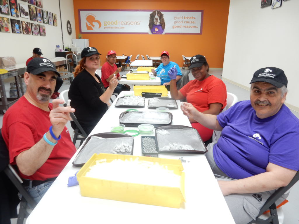 Eight workers sit at a long table meticulously packing supplies for a lab company.