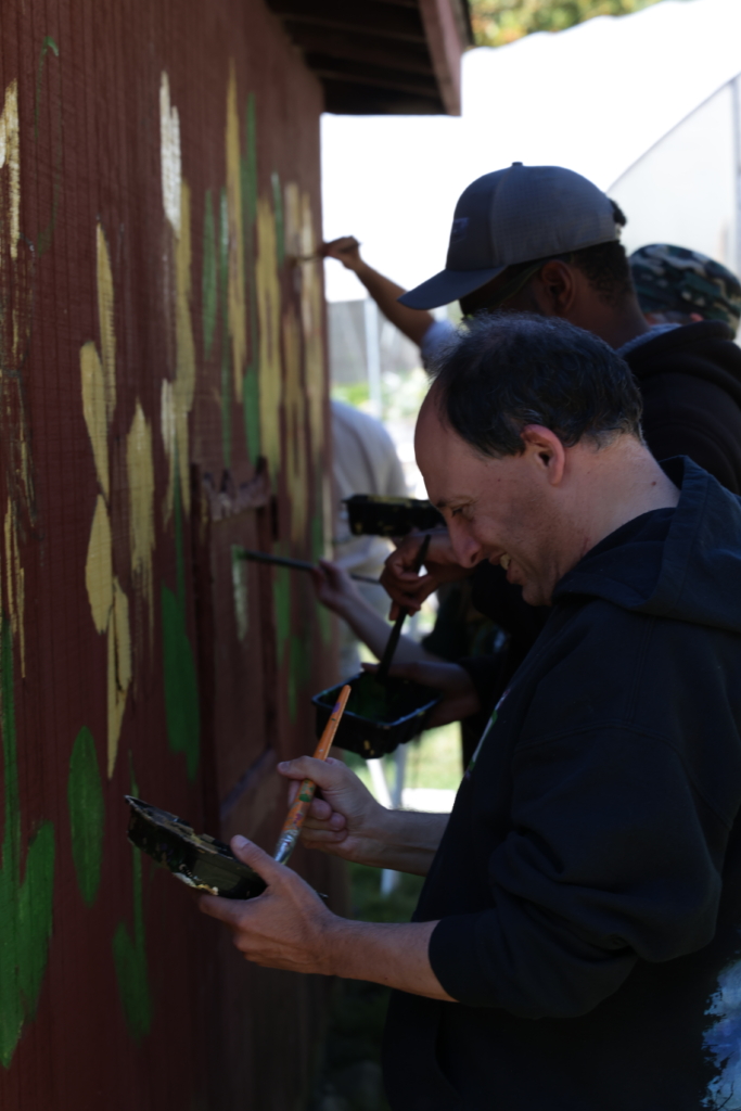 A man smiles as he loads his brush up with paint as he works on the sunflower mural.