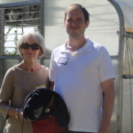 A mother and adult son stand outside in front of the greenhouse