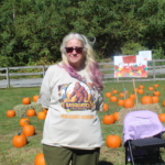 A staff member poses in front of the pumpkin patch and wears a graphic tee shirt with a sasquatch on it.