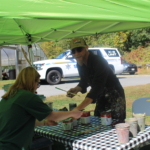 Artist Brian Zickafoose hands a palette of paint to a participant under a tent.