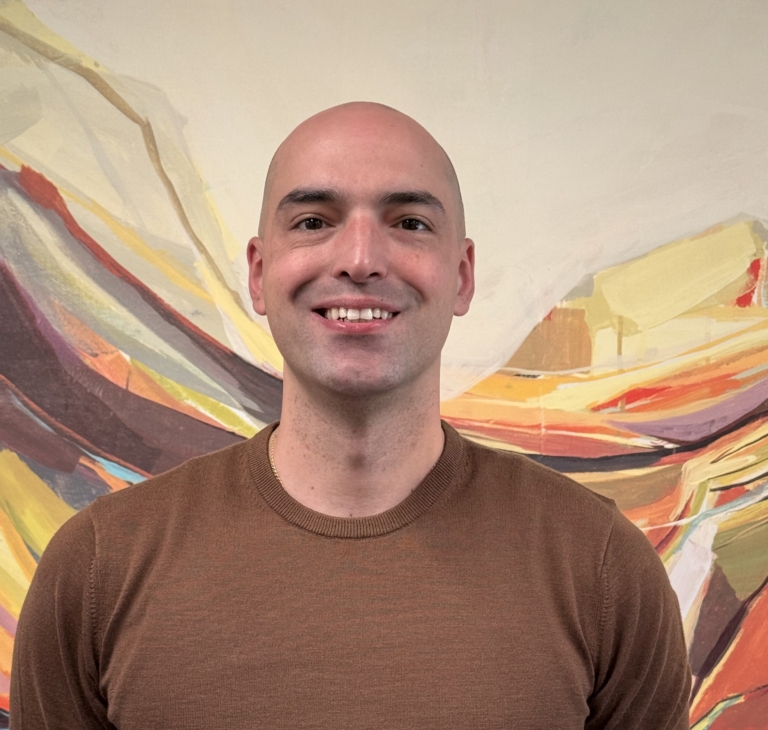 Group Day Hab Manager Frank DiMaggio stands in front of an abstract painting and wears a brown shirt.