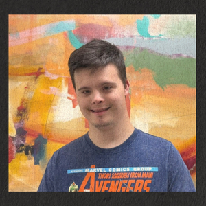 Raymond stands in front of an abstract painting and wears an Avengers Tee shirt.