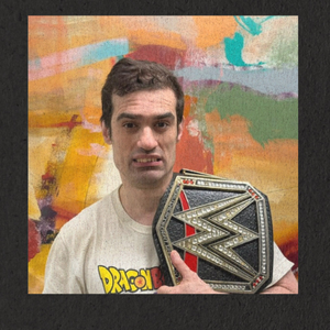Justin holding a wrestling belt and wears a white graphic tee while standing in front of an abstract painting.