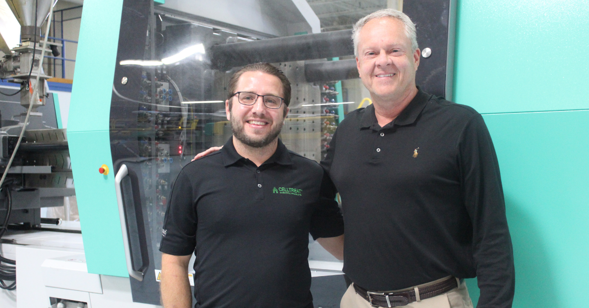 Director of Manufacturing at Vista Labs, Jon Benack stands with Community Relations Manager Joe Conti in front of a plastic molding machine.