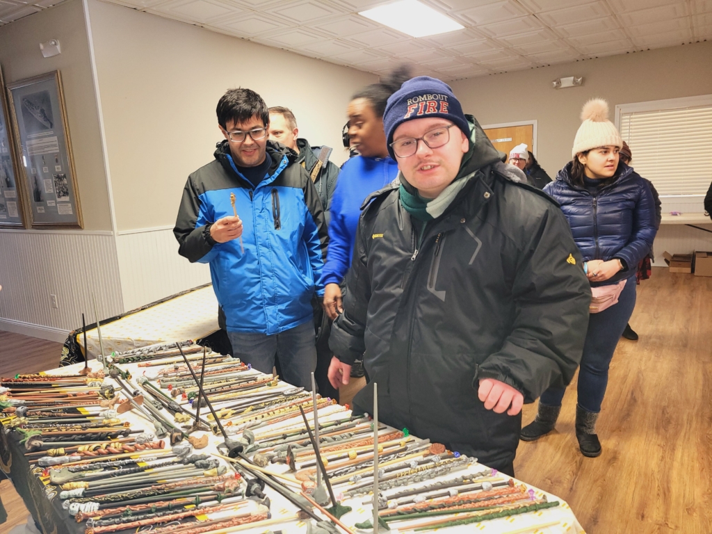 People in the CBS day services stand in front of a table laid with hand made Harry Potter style wands. The wands were made by the group for the Harry Potter gala.