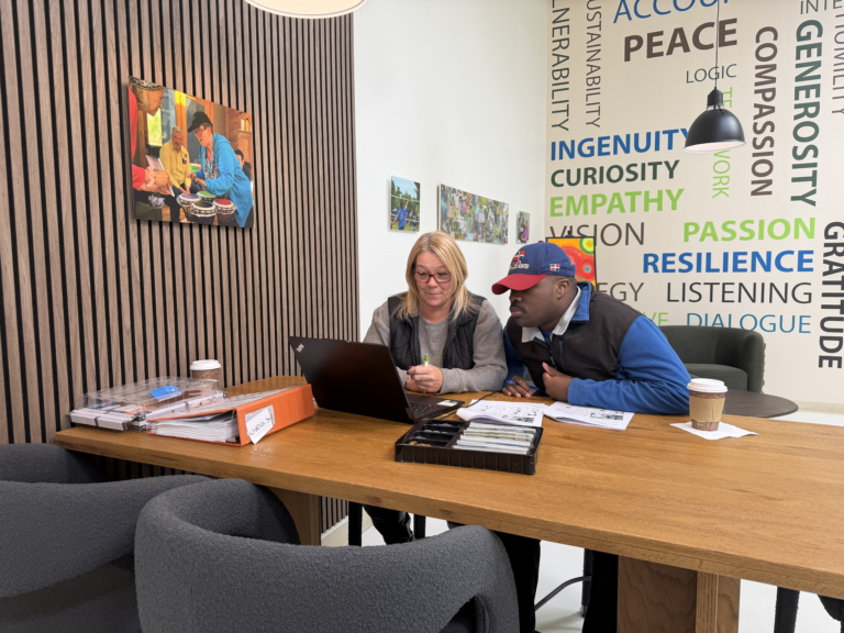 A job coach and a person seeking to develop job skills sit at a long wood conference table at the Impact Center for Learning. They are surrounded by new comfortable modern chairs, walls filled with art and wood sound proof paneling.