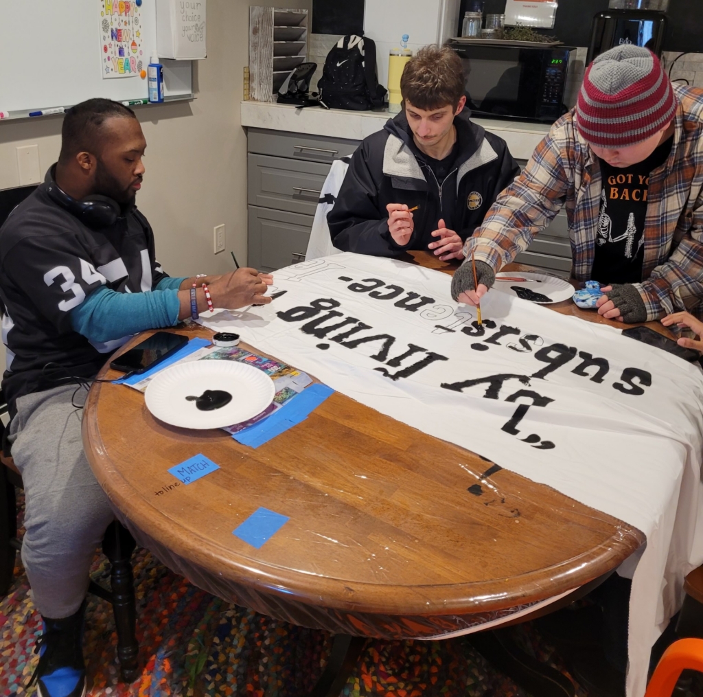 3 Men supported by CBS work together to paint a sign for the Rally in the Valley.
