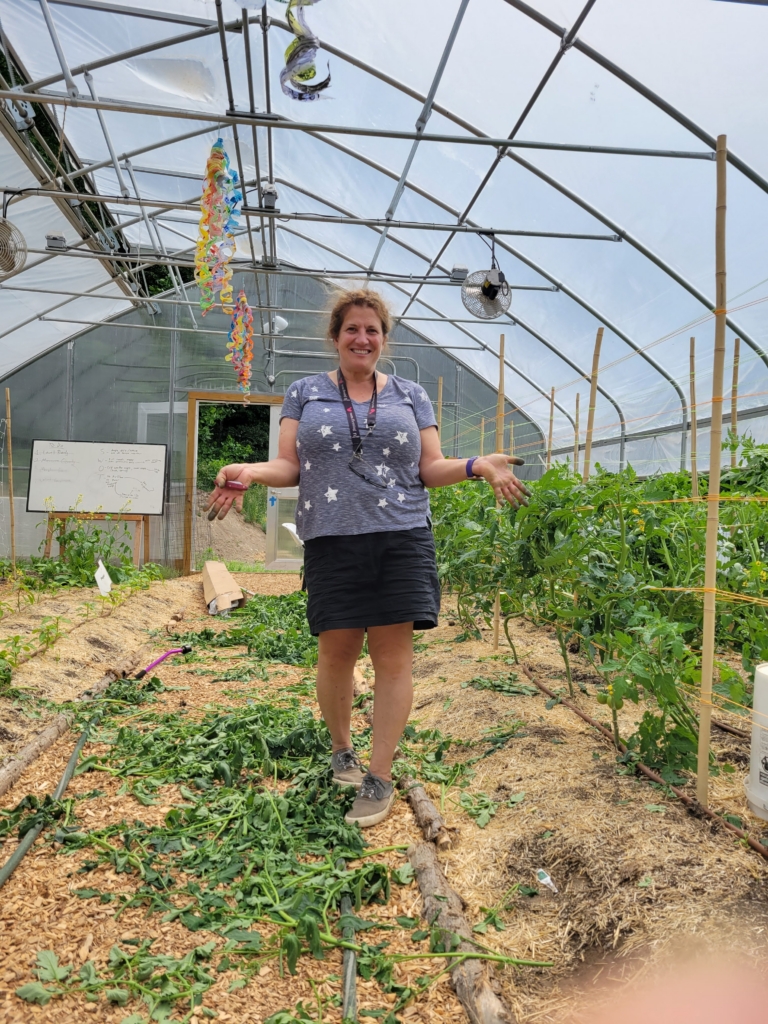 CBS Agricultural Coordinator at Cultivating Dreams Farm stands in the greenhouse amid new spring growth.