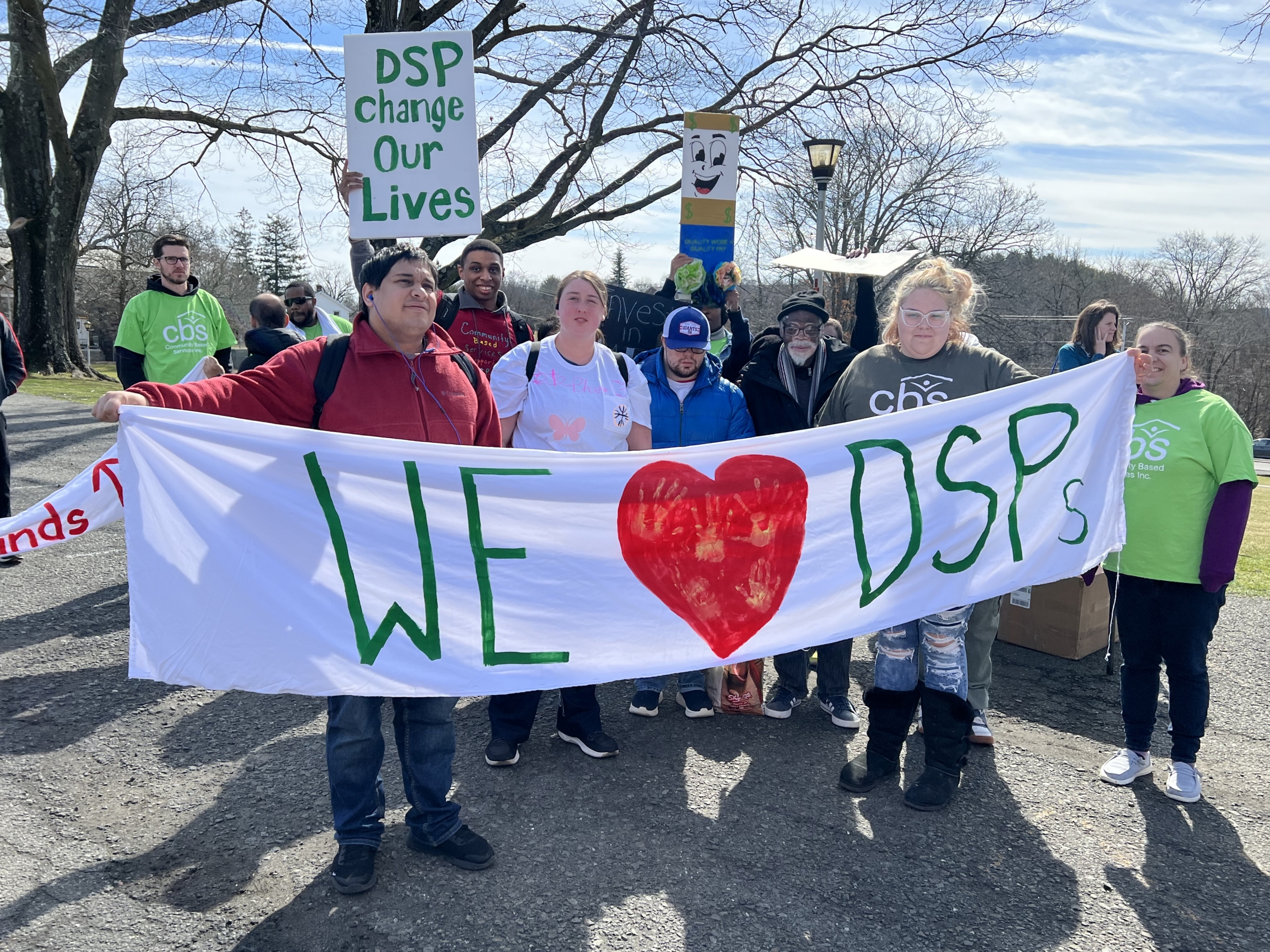 People supported by CBS hold a large banner that says We Love our DSPs while at the Rally in the Valley.