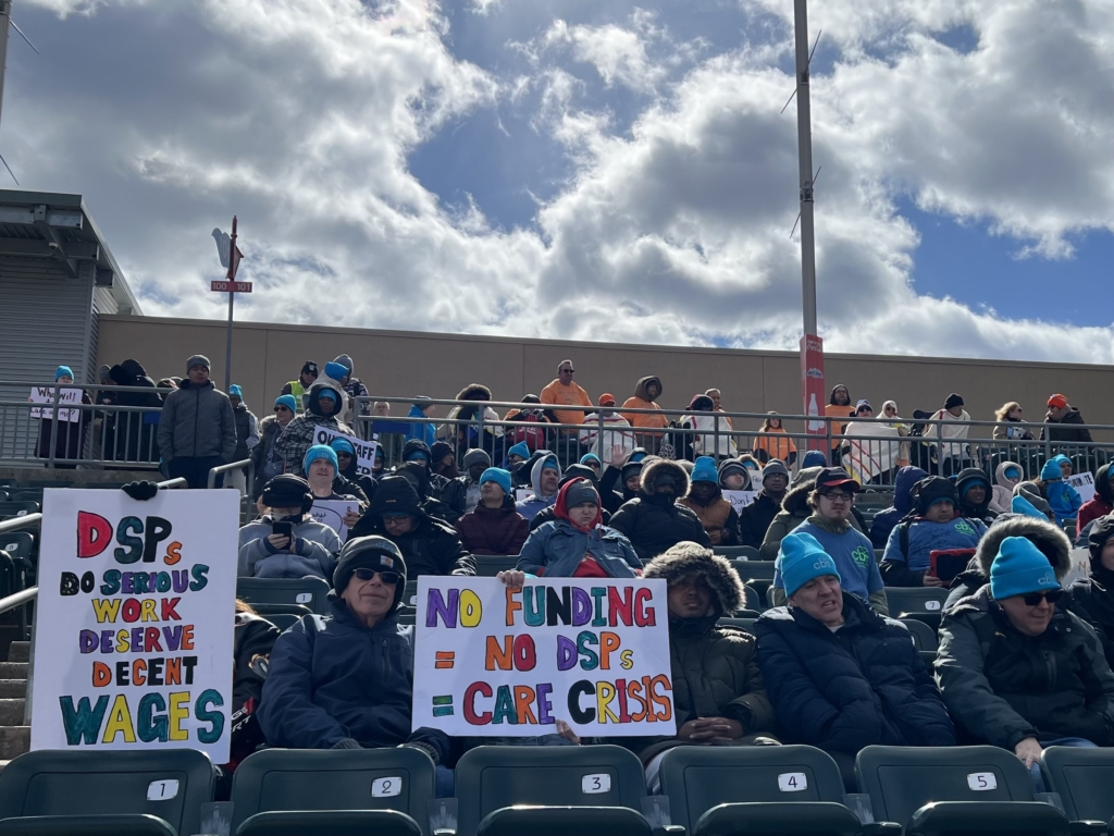 A large crowd of supporters gathers at the Rally in the Valley. A small group in the forefront hold large signs.