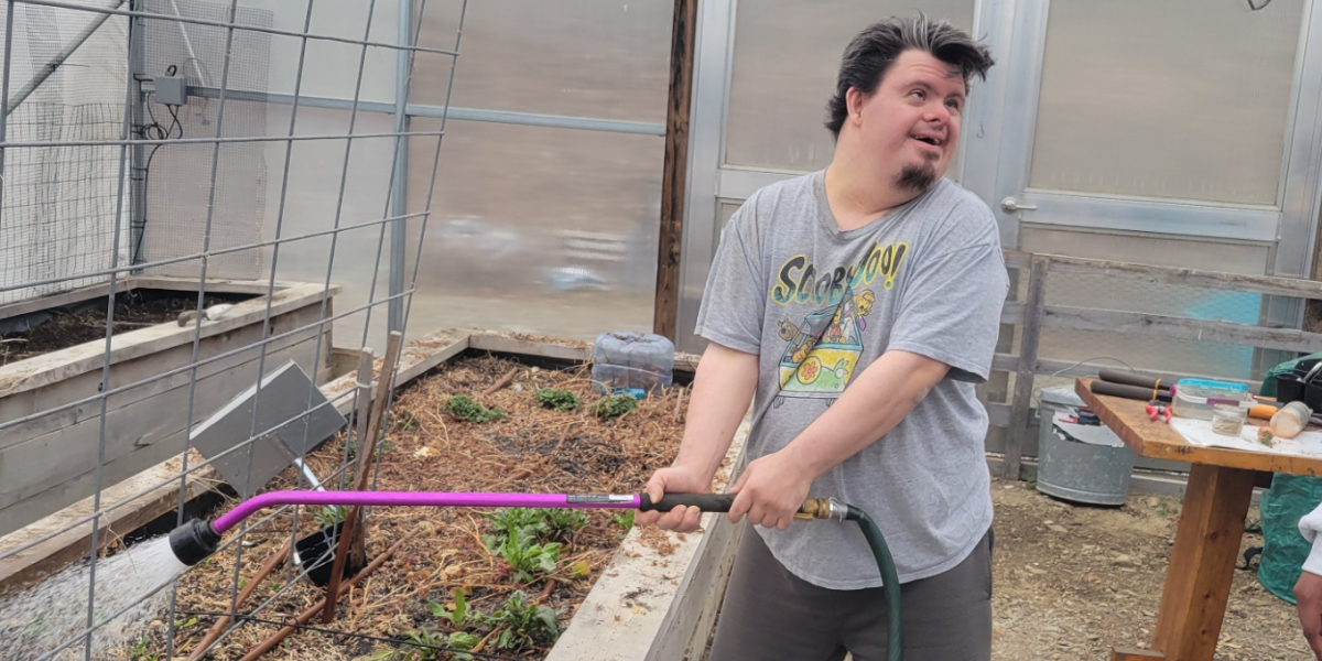 A person in the agricultural program at Cultivating Dreams Farm enjoys watering the young plants in the greenhouse.