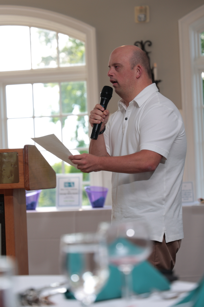 Brandon T. addresses the guests in the dining room of Salem Golf Club with a spoken word performance. He holds a microphone in one hand and his poem in the other.