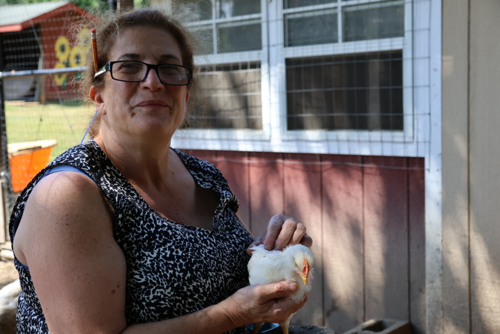 Olimpia Bernarnd, agricultural coordinator of Cultivating Dreams Farm, sits outside the red barn and holds a white chick.