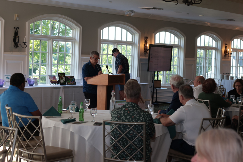Chuck Newman at the podium announcing live auction items while dinner guests look on in the dining room of the Salem Gol f Club.