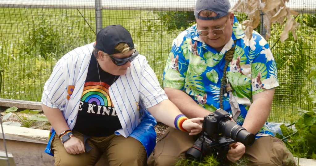 Jon Harrison, photography teacher at InterArts holds a camera while a student interacts with it in the garden at Cultivating Dreams farm.