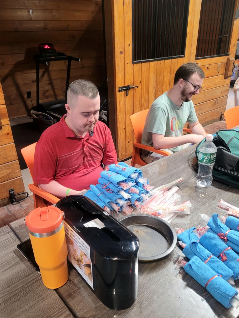 Two men sit at a table in the Cultivating Dreams barn as they work on packing items for Fruits of Caring.