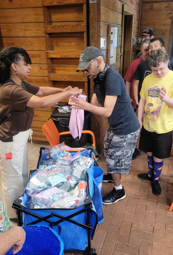 With the assistance of a direct support professional, a group day hab participant loads packs into a large container for delivery to those in need as part of the Fruits of Caring 9/11 service project.