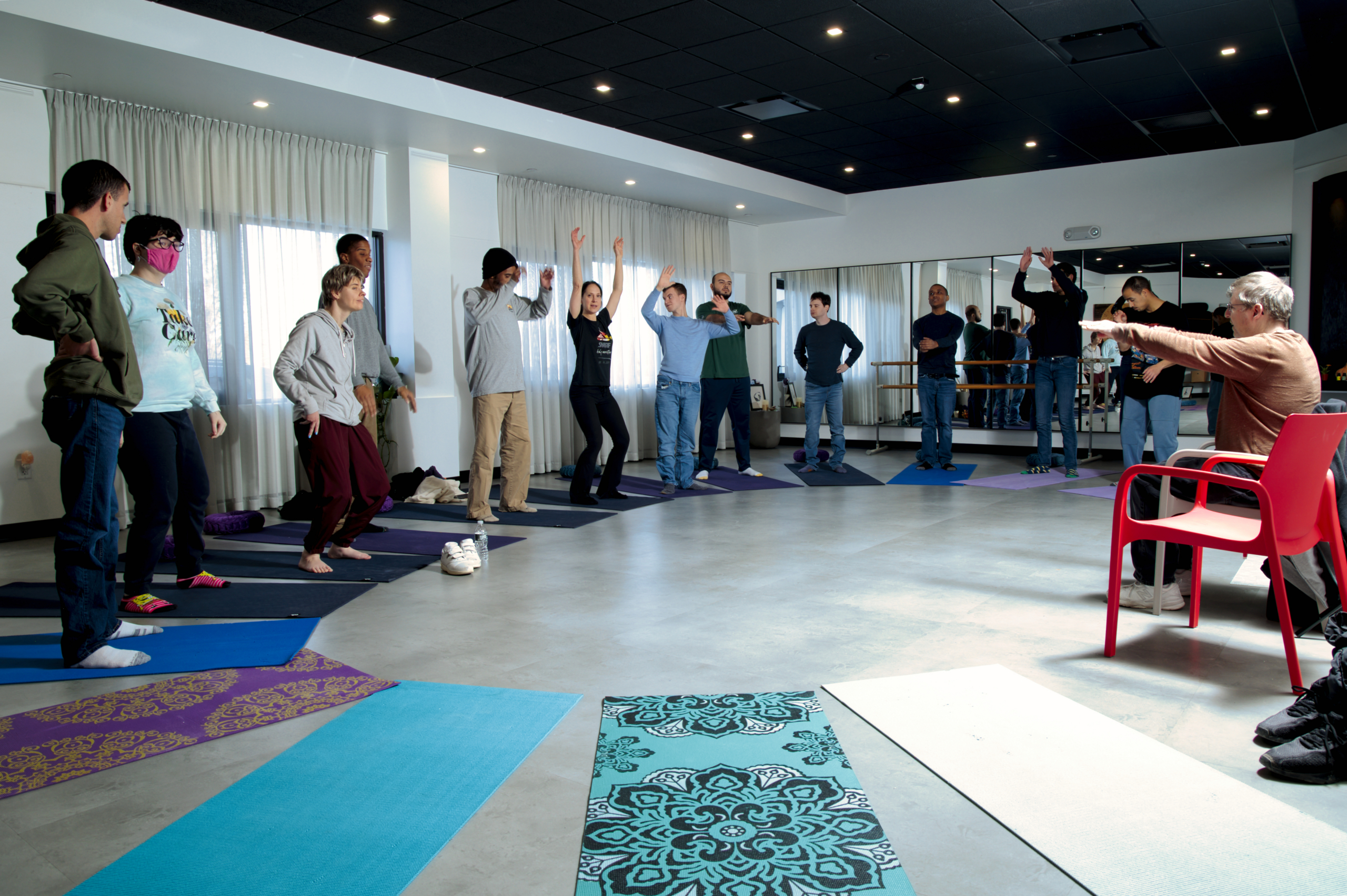 The yoga class at Hudson Valley InterArts poses in the large yoga studio. They stand on yoga mats in tree pose.
