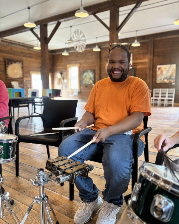 A man in the CBS Group Day Hab program at InterArts North sits at a mini marimba xylophone with sticks in hand while smiling.