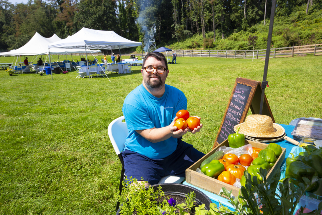 Man is sitting outside holding tomatoes in his hands and smiling.